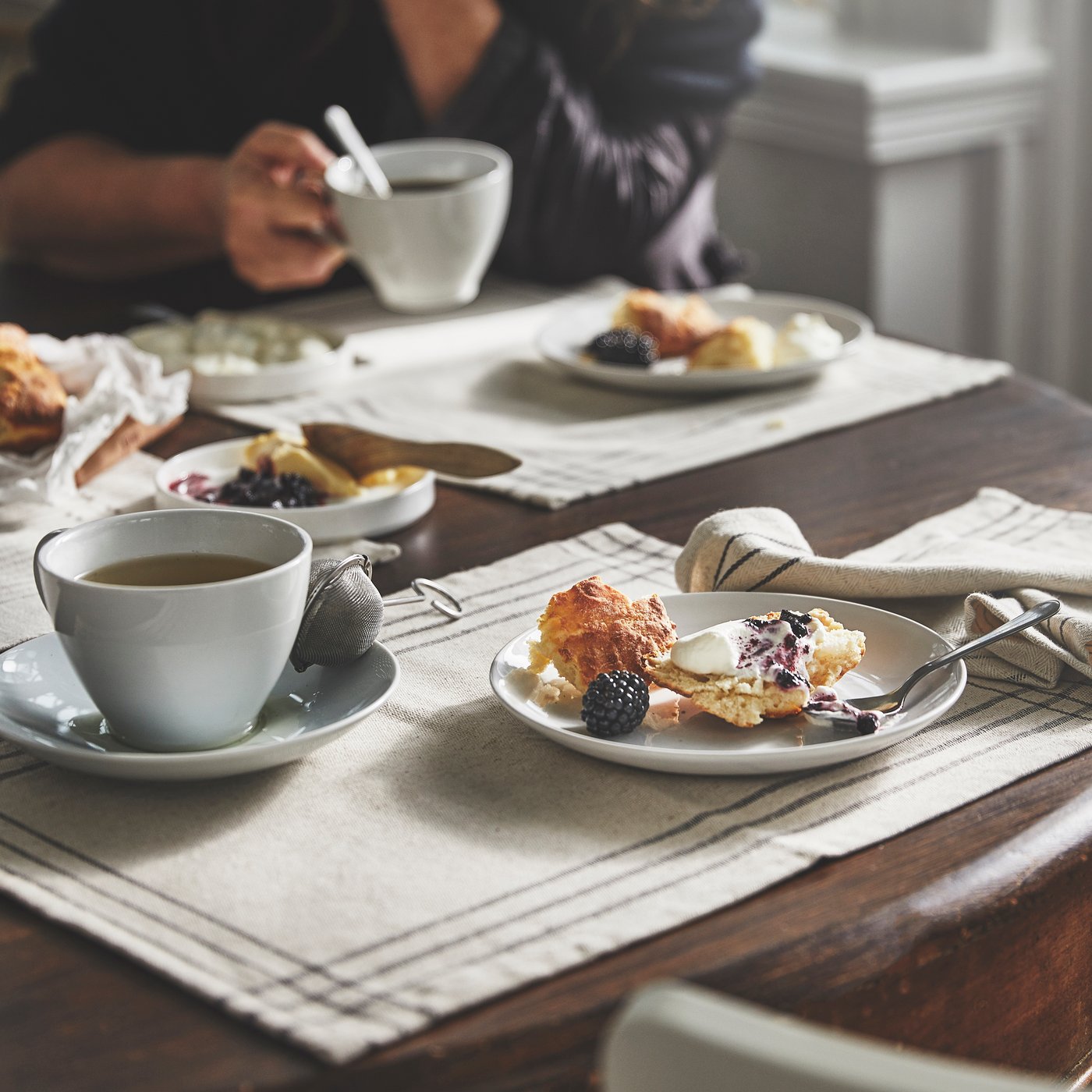A cozy breakfast scene with croissants, fresh berries, and coffee served on white plates and cups on a wooden table with striped linen placemats.