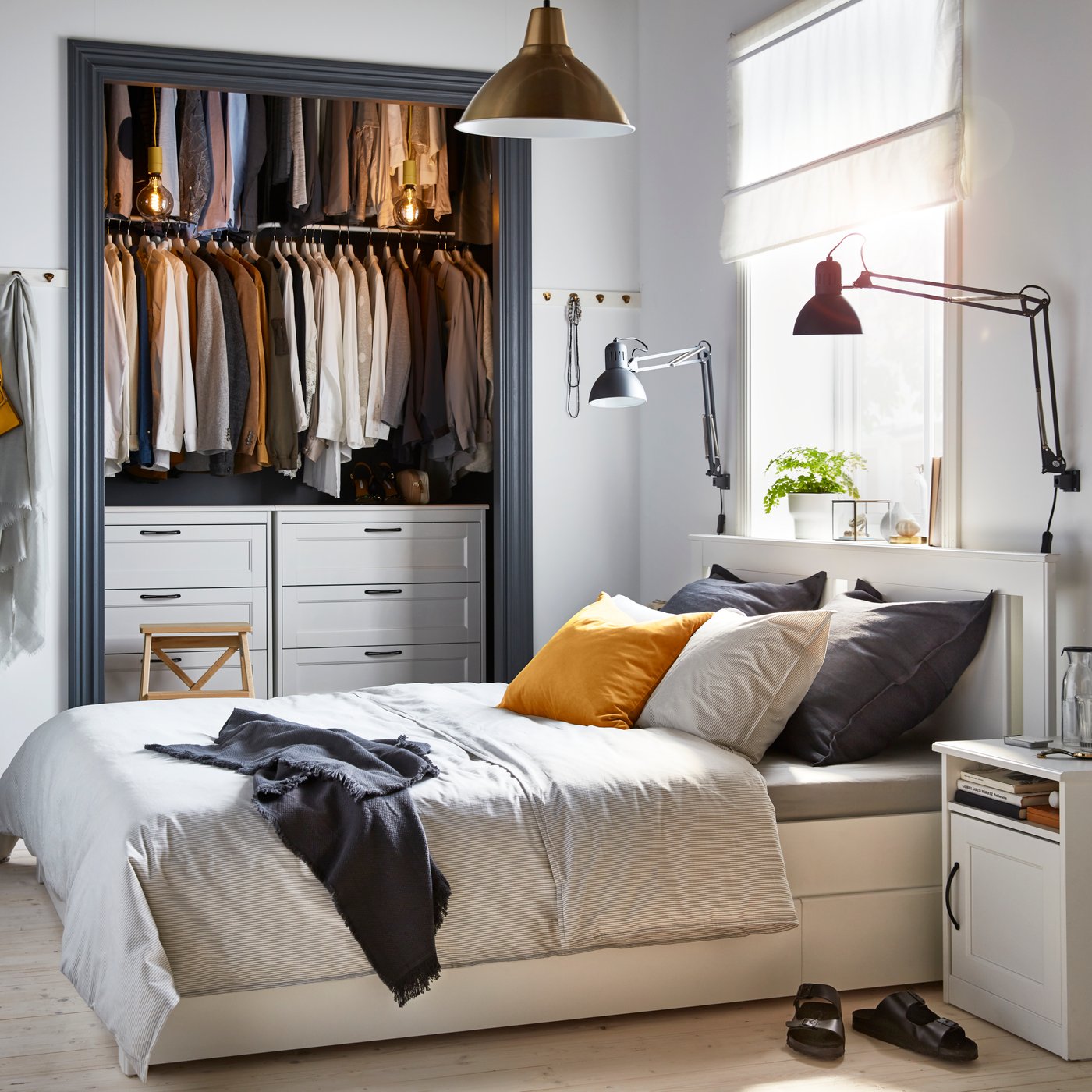 Ein weißes Bett mit grauere Bettwäsche, einem Nachtkästchen und einer Kommode im Einbauschrank im Schlafzimmer.