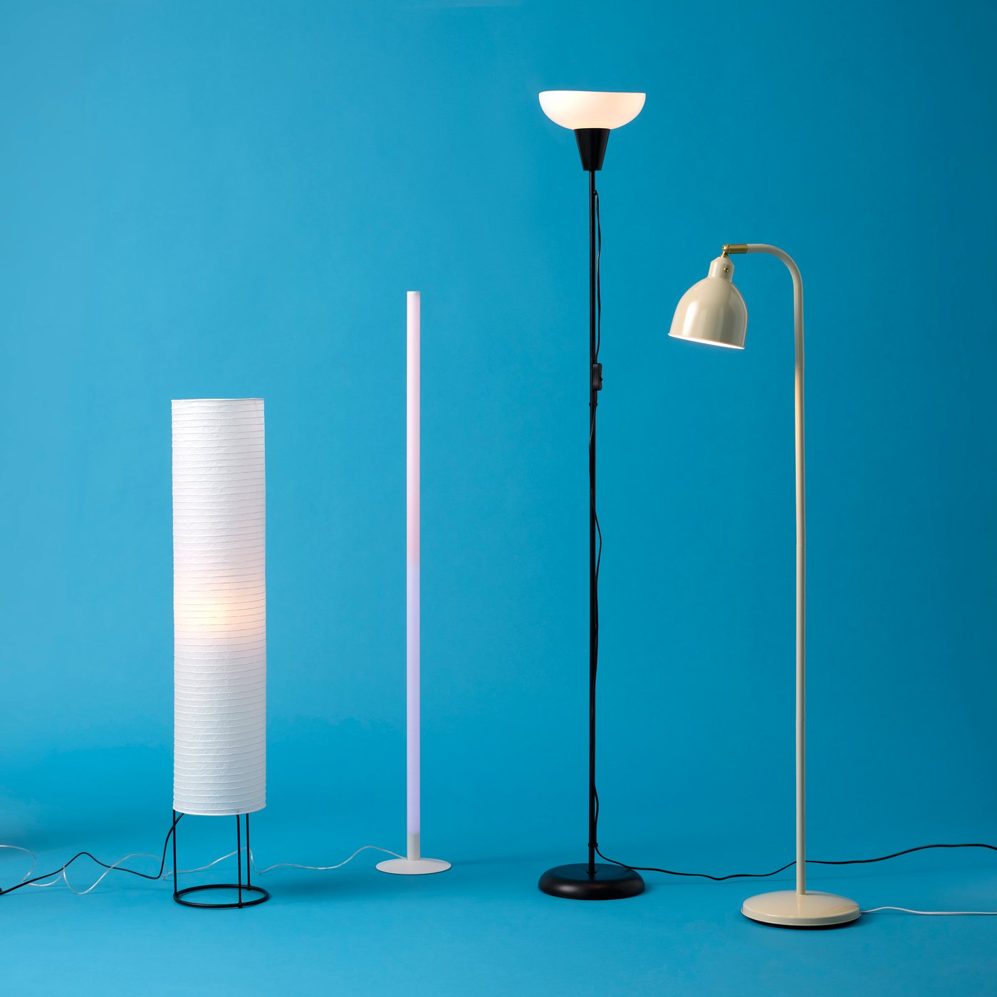 An arrangement of four lit floor lamps, one of them a TÅGARP floor uplighter, placed side by side against a blue background.
