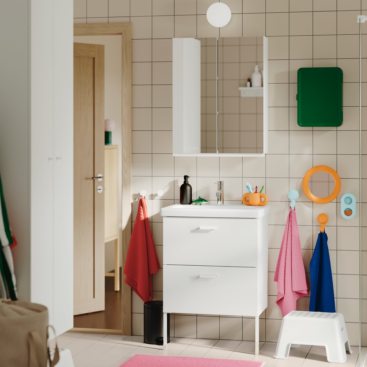 A tiled bathroom featuring the white TVÄLLEN/ENHET wash-stand with two drawers, wall-mounted with colourful towels nearby.
