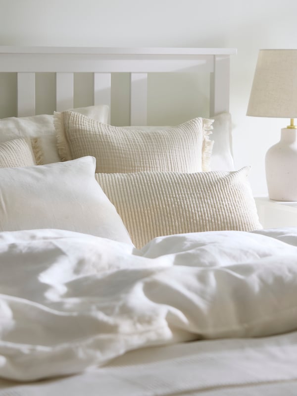 The head of a white HEMNES bed covered in white DYTÅG bed linen and cushions in covers including a VALLKRASSING cover.