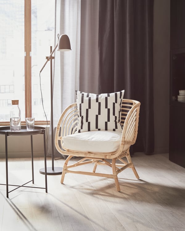 Un fauteuil en bois clair au milieu d’une pièce près d’une lampe SKURUP en noir et d’une table d’appoint. 