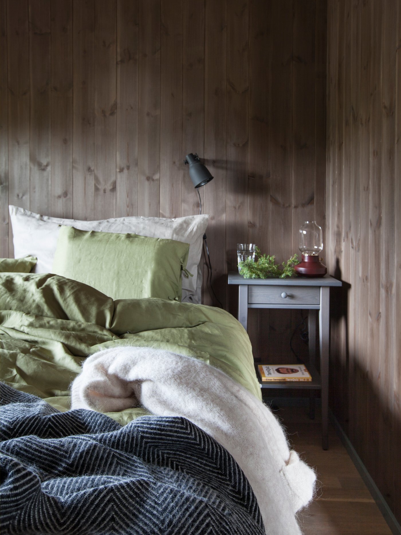 En seng redt med bløde og mørke tekstiler i et soveværelse i et sommerhus. 