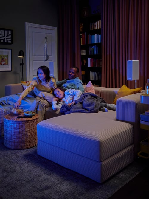 Eine Familie hat es sich auf einem JÄTTEBO 3er-Sitzelement mit Récamiere bequem gemacht, u. a. mit einem EVALI Plaid, einem LANGSTED Teppich und einem TOLKNING Hocker mit Aufbewahrung.