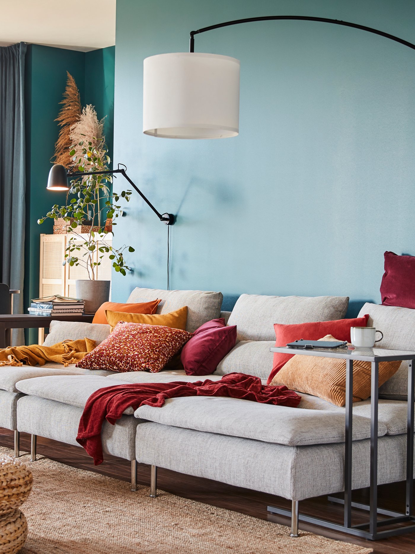 Chaise longues beige, una pantalla fijada a una lámpara de pie arqueada, una lámpara de pared, varios cojines y un soporte para portátil.
