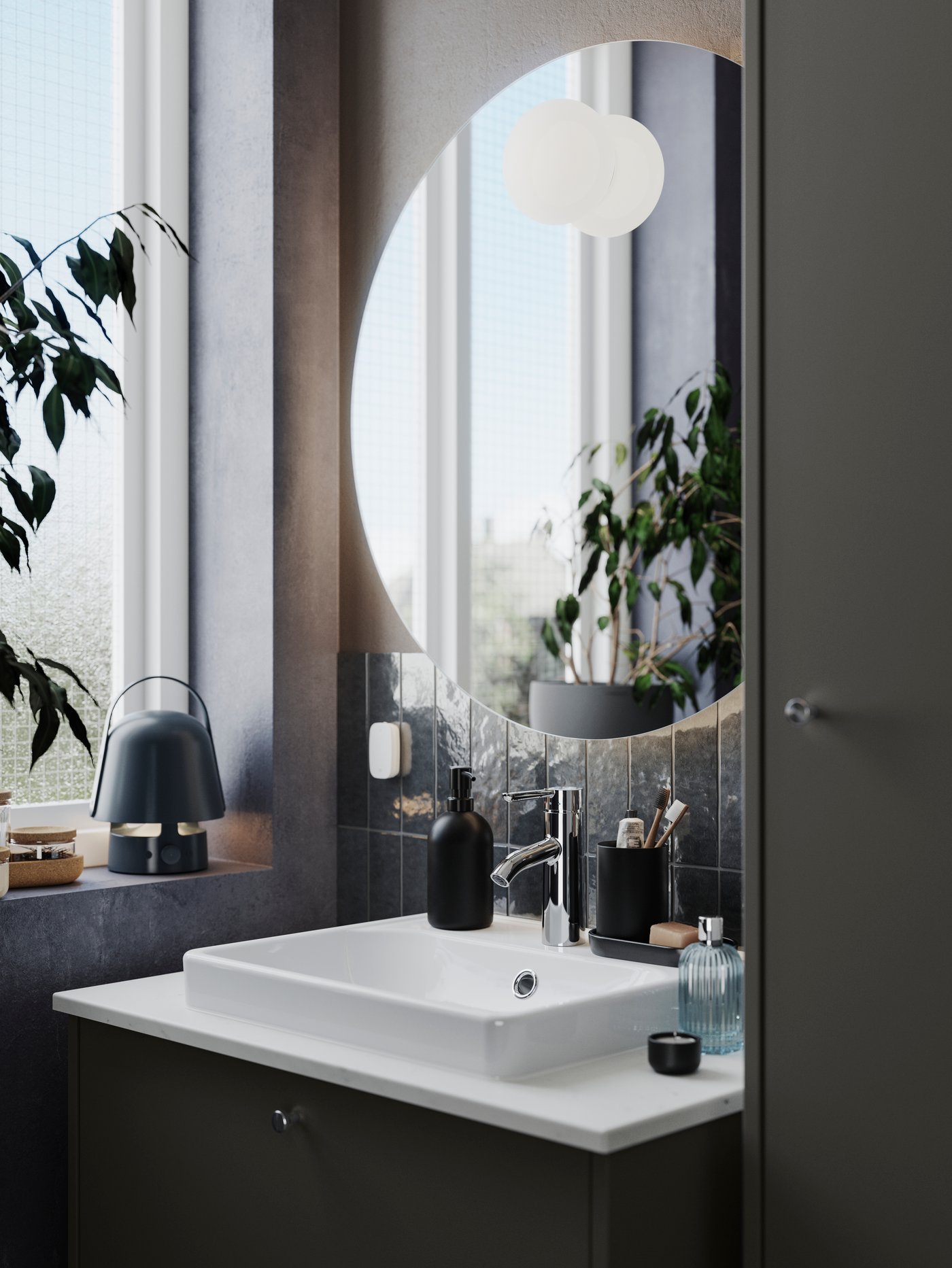 A round FAXÄLVEN mirror with built-in lighting all around is placed on a bathroom wall above a dark grey HAVBÄCK washstand.