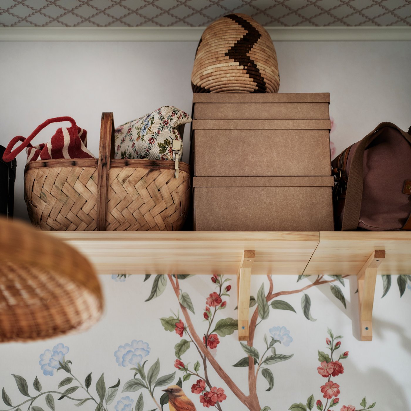 Ovanpå en vägg nära taket finns en TRANHULT-hylla i asp som håller GÄRDESGÅRD förvaringslådor med lock och korgar.