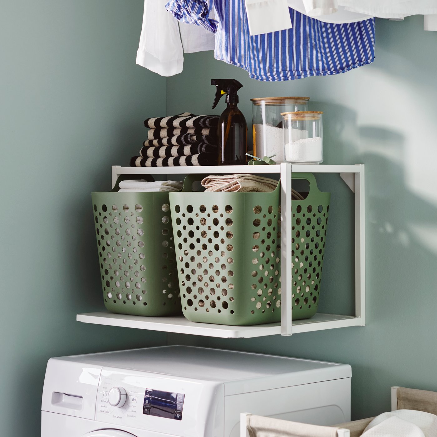 Un barattolo EKLATANT in vetro trasparente/bambù con coperchio e due ceste verdi su uno scaffale ENHET bianco