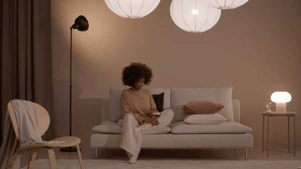 A lady is sitting on a sofa in the living room with various types of lighting around her.