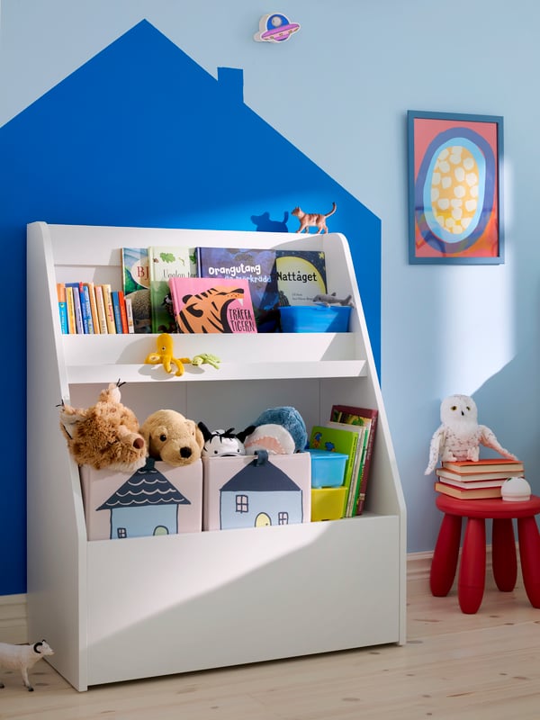 Close-up of BERGIG book display with storage, full of books and soft toys, in a children’s room with a light blue wall.
