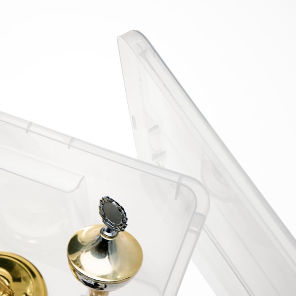 A close-up of a transparent SAMLA box with lid. Inside, we see part of a sport trophy.