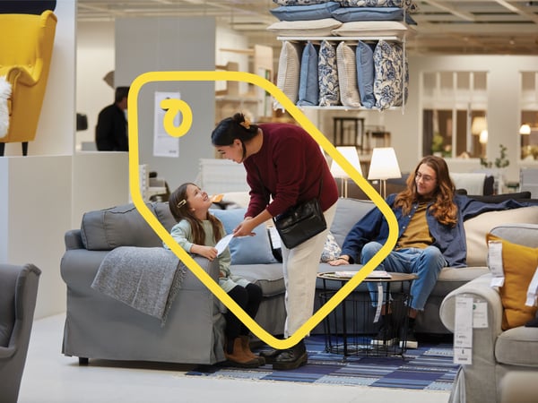 Et lille barn og to voksne i et IKEA varehus prøver en grå sofa.