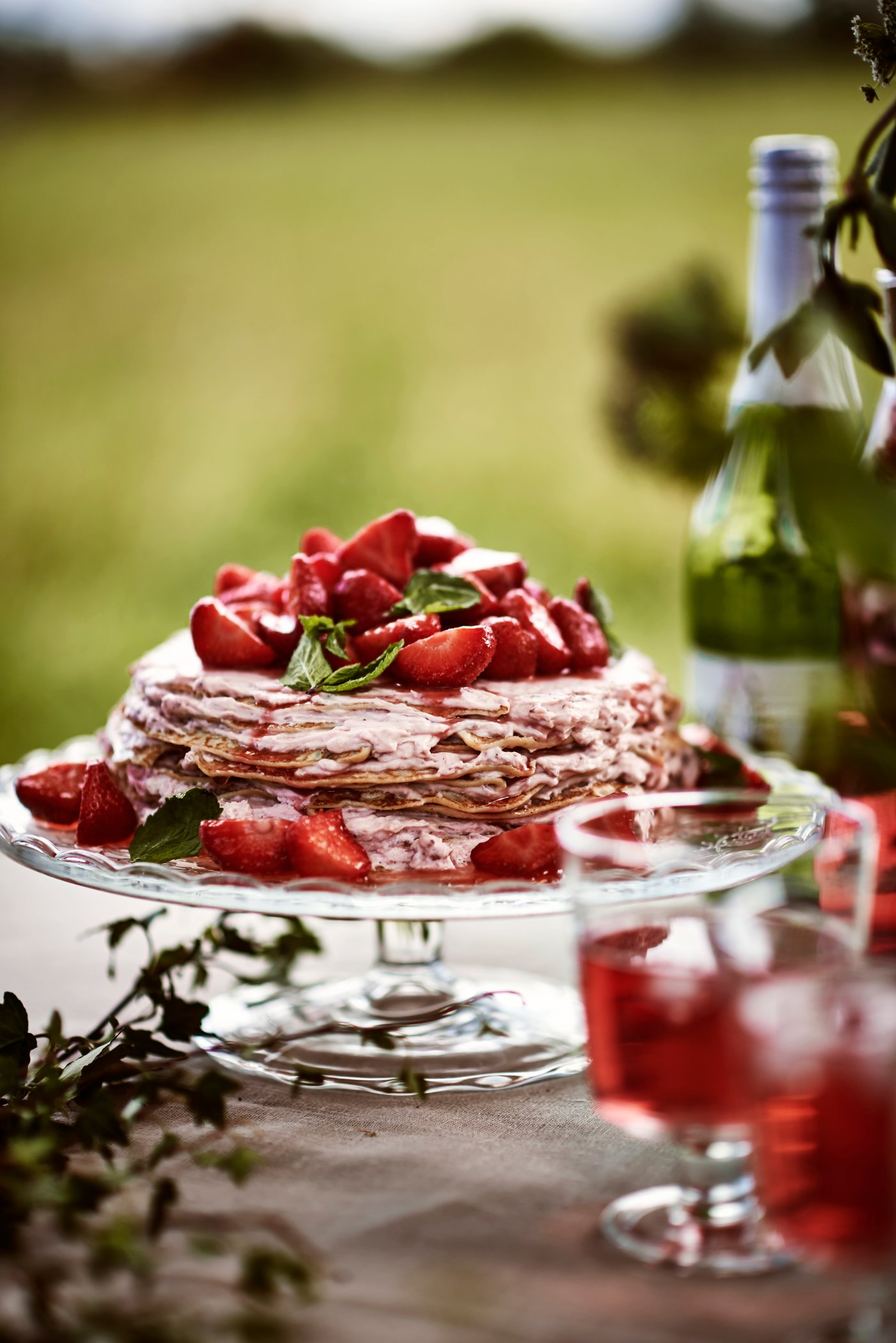 A cake and cake stand sit on a table with a wine bottle