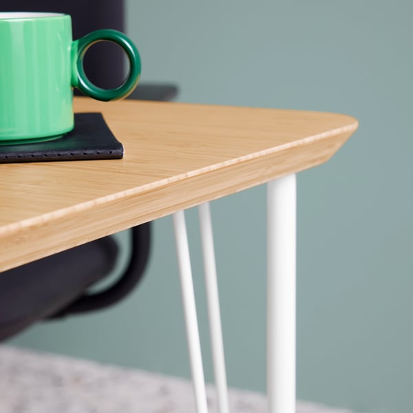 A close-up of the bamboo ANFALLARE tabletop and white KRILLE legs. On the desk is a black notebook and a white/green mug.