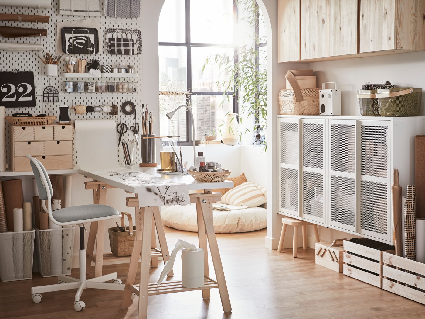 A bright home office with a white desk, a white/yellow green swivel chair and a white pegboard with crafting materials.