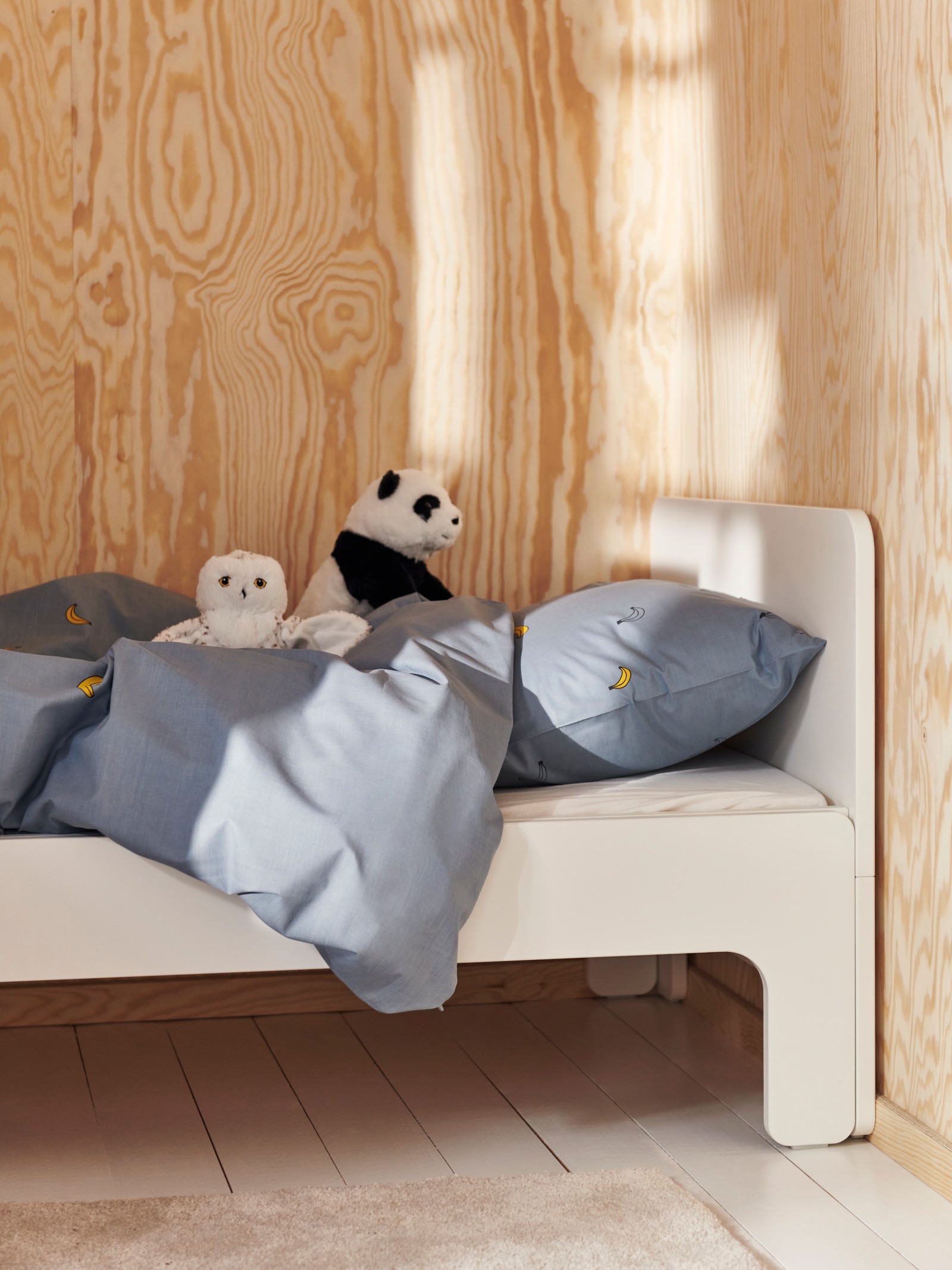 The top end of a white SLÄKT extendable bed with a white LEN fitted sheet and banana blue VÄNKRETS bed linen on it.