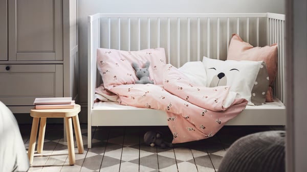 Habitació infantil bàsica amb una cadira de fusta i un bressol amb roba de llit amb estampat rosa.