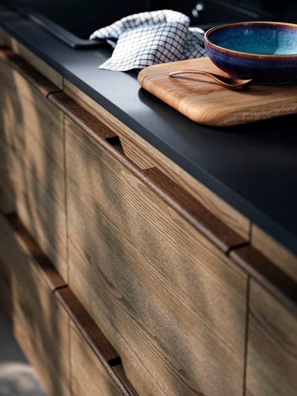 STENSTA dark brown ash veneer drawer fronts, a sleek black countertop, with a wooden cutting board and ceramic bowl on top.