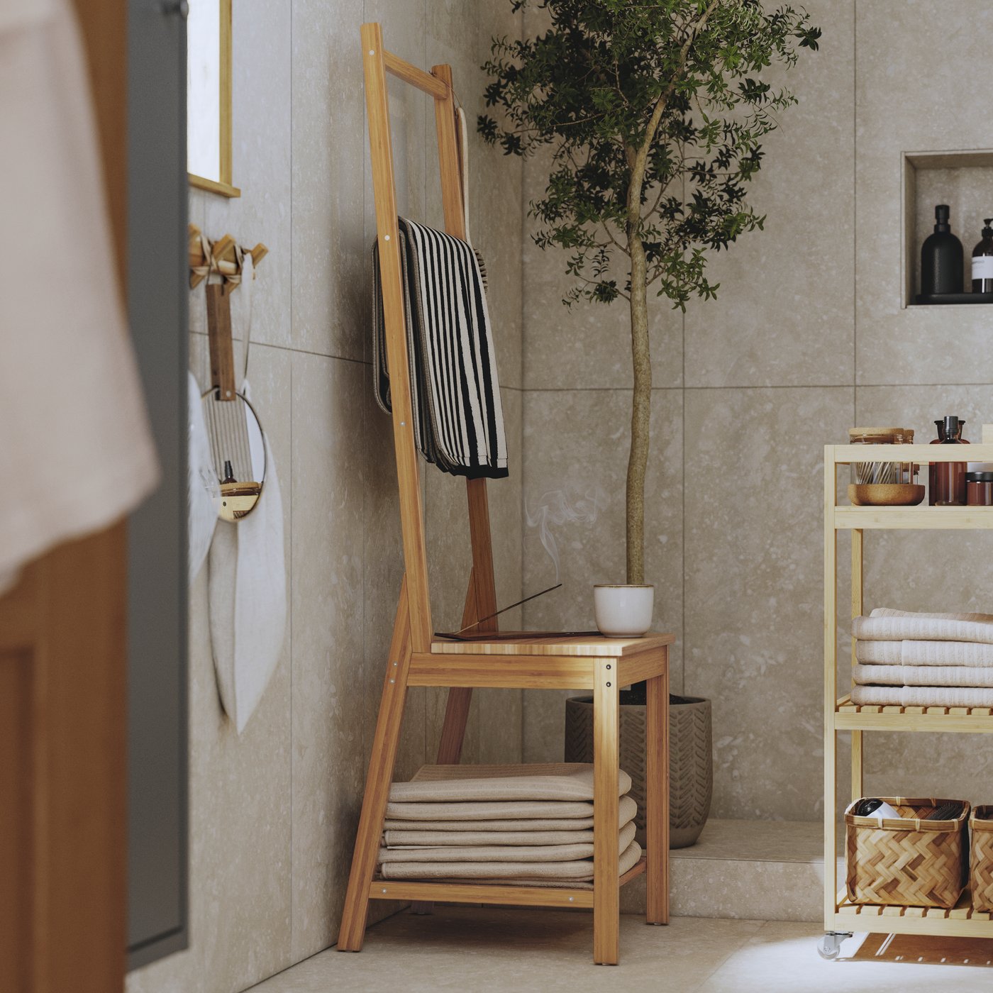 Ett soligt badrum med RÅGRUND handdukshängare och vagn i naturlig bambu fylld med handdukar och spaprodukter. En växt.