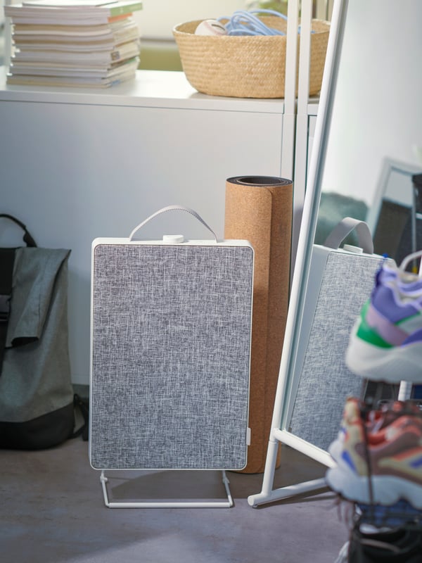 A FÖRNUFTIG air purifier sits on the floor by a mirror and a yoga mat. A shelving unit with books and a basket are behind it.