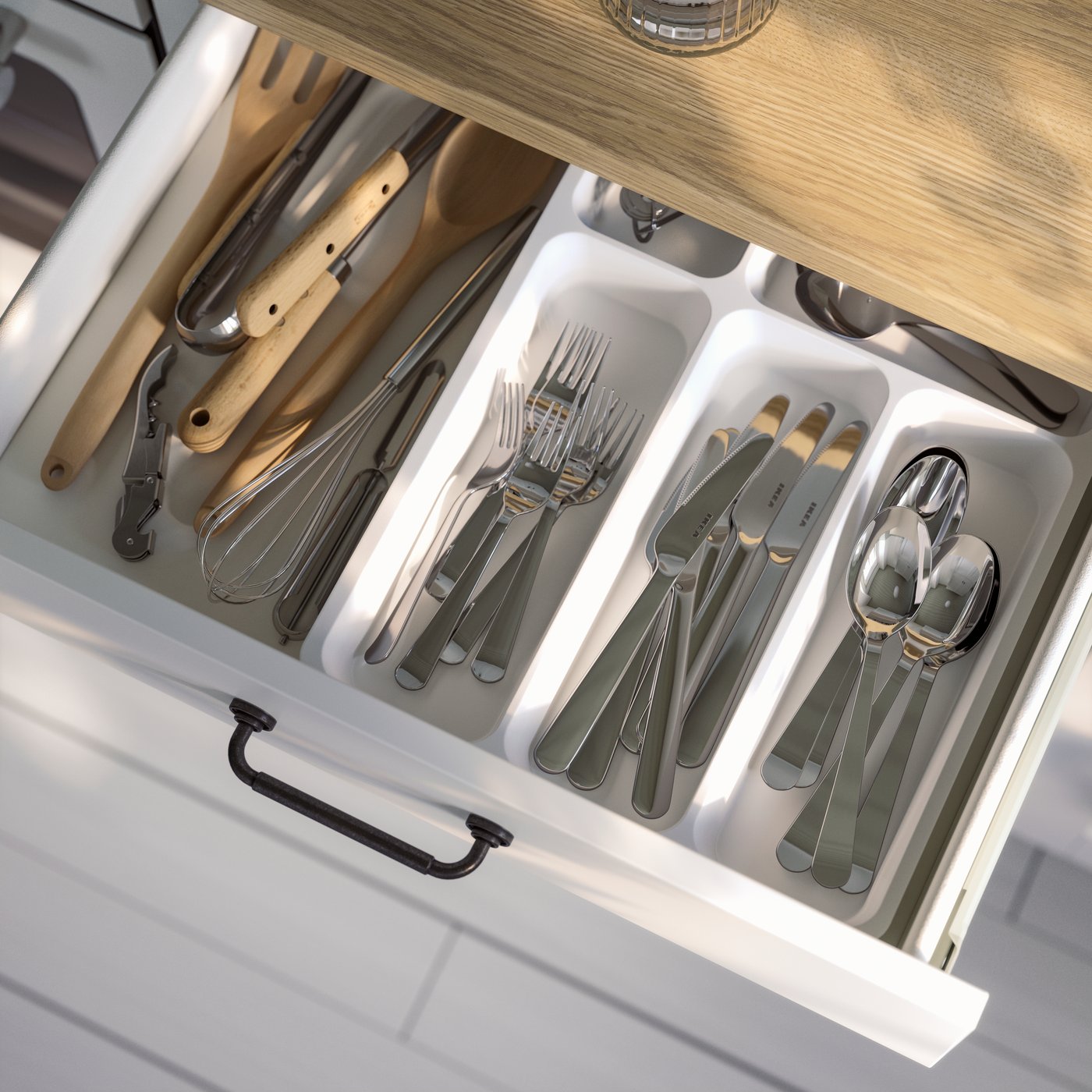 A white STÖDJA cutlery tray is placed in a pulled-out drawer in a KNOXHULT cabinet and there are utensils stored inside.