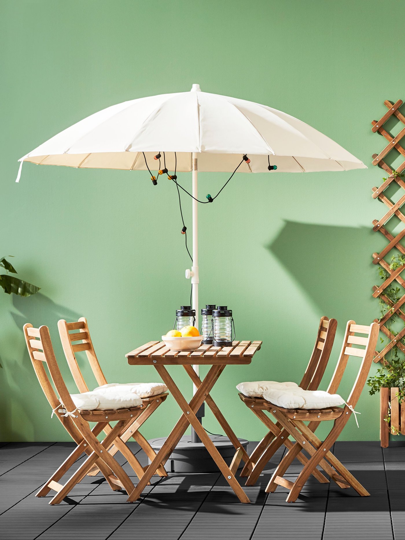 Tavolo e 4 sedie pieghevoli ASKHOLMEN in legno con sedie beige e ombrellone, allestiti all’aperto.