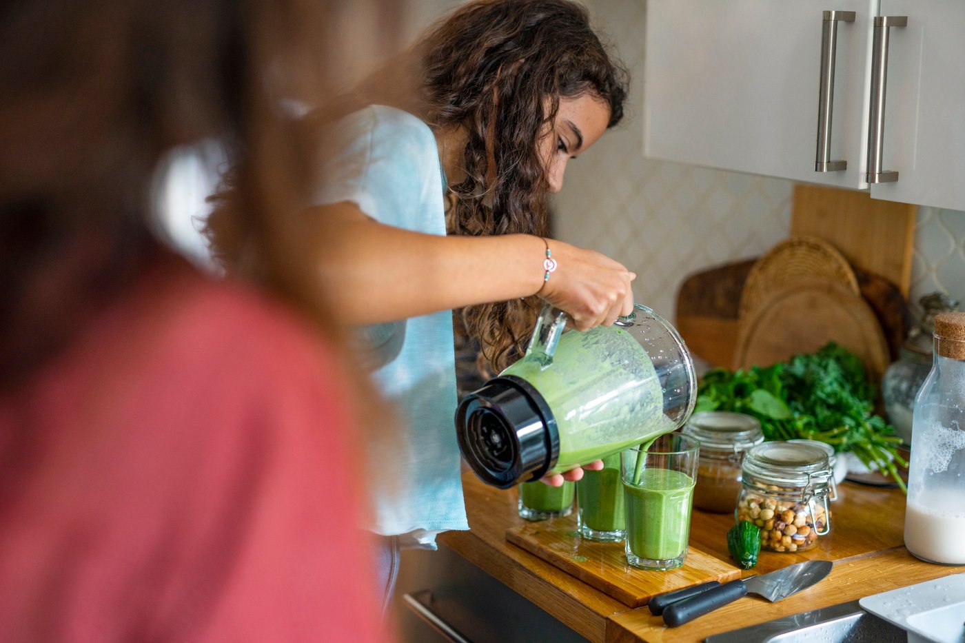 Teenage girl pouring a freshly made green smoothie from a mixer into three POKAL glasses.