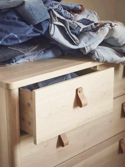 The top drawer of a BJÖRKSNÄS chest of drawers that is slightly open, with a pile of folded denim clothing on top.