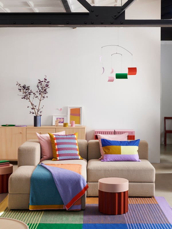 A TESAMMANS side table stands on a colourful rug, in front of a sofa with two TESAMMANS cushion covers and a throw on it.