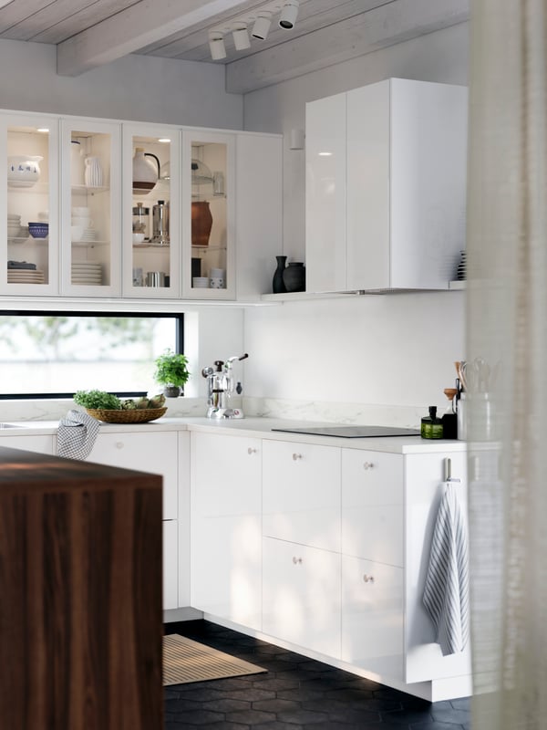 A bright kitchen with glossy RINGHULT fronts and cabinets with HEJSTA glass doors has a kitchen island and a picture ledge.