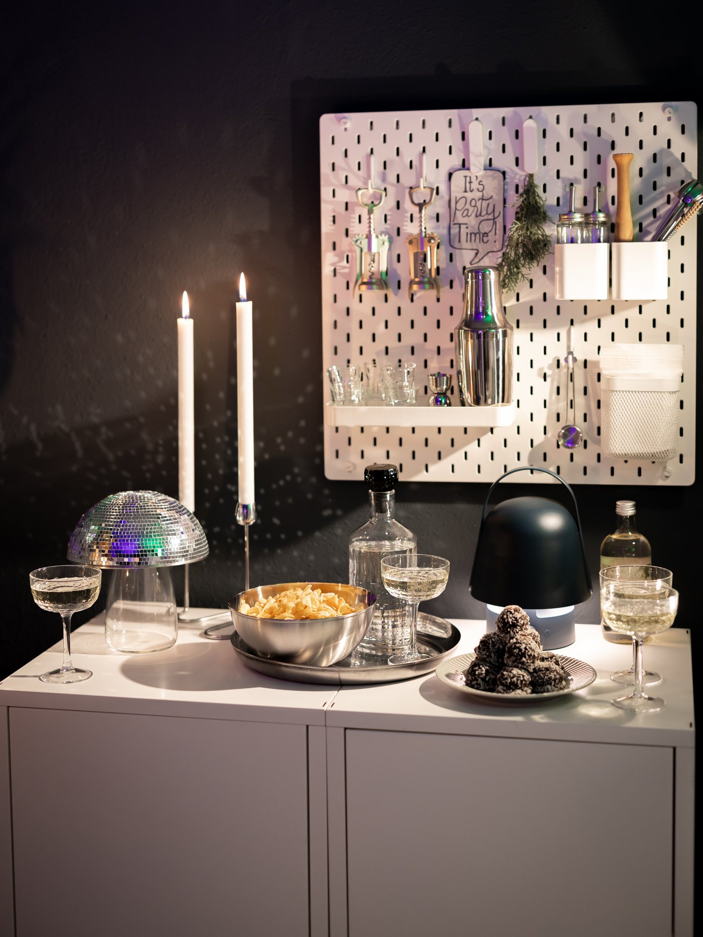 A white cabinet topped with bowls of food and snacks for New Year’s Eve. One bowl is covered in disco stickers, making it look like a half disco ball.