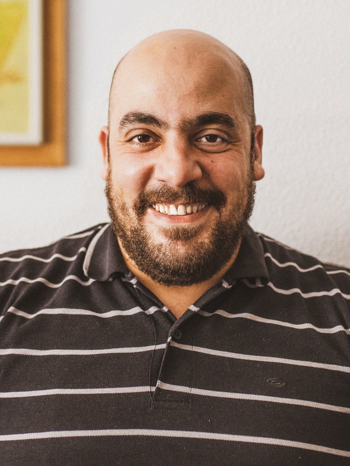 Tarek, a Syrian refugee and IKEA Spain co-worker, smiling, wearing a brown and white striped shirt.