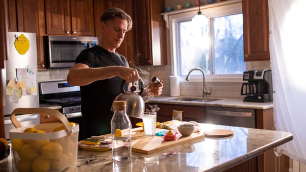 Man preparing a fresh lemon juice drink in a kitchen full of natural light.