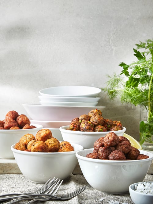 Vegetable balls, meatballs, chicken meatballs, and salmon and cod balls, placed in four, white bowls.