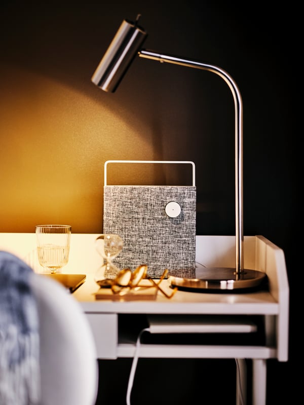 The right corner of a white HAUGA desk with a lit VIRRMO work lamp and a ENEBY Bluetooth speaker.