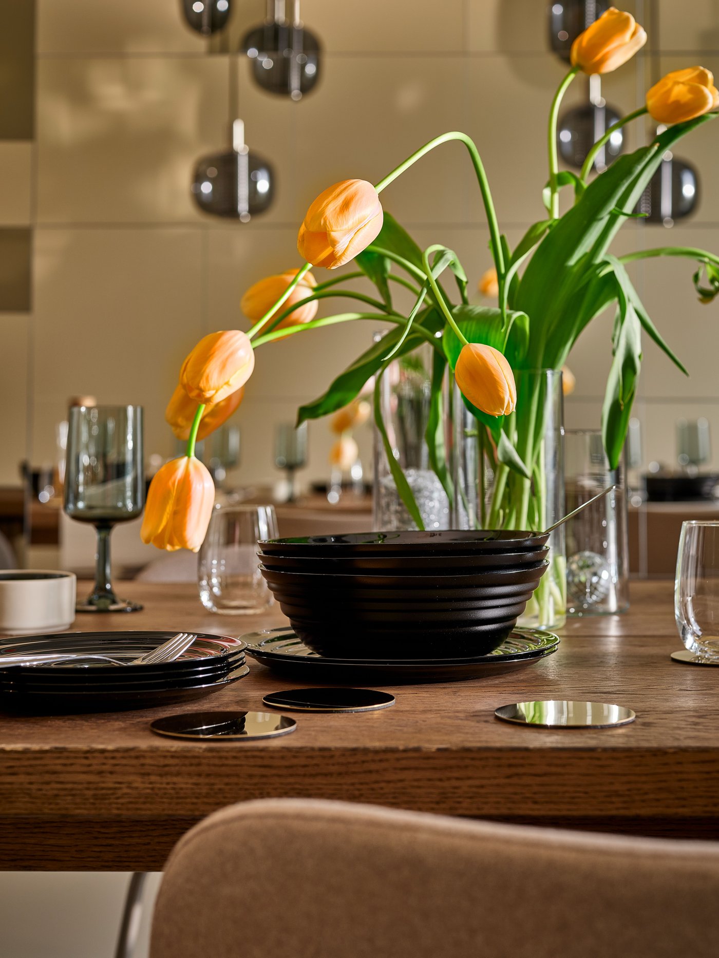 Dining area featuring a black NÄTBARB bowl set on a wooden table next to a CYLINDER vase with flowers.