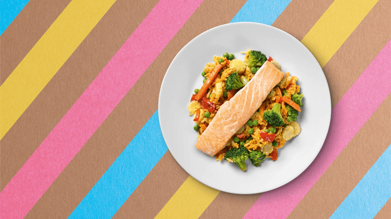 Ein Teller mit Reis, Gemüse und Lachs auf buntem Untergrund.