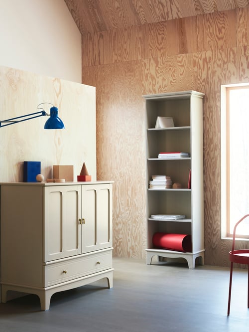 Un rangement LOMMARP beige clair avec un tiroir et deux portes dotées de poignées tombantes et une bibliothèque assortie dans une pièce aux murs en contreplaqué.