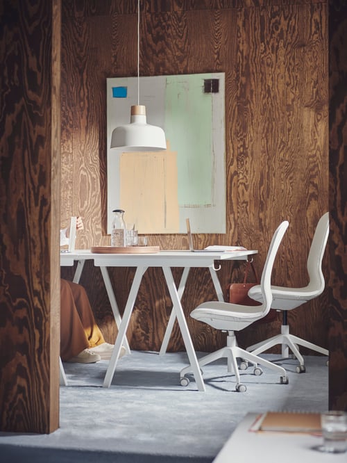 Modern workspace with large artwork, beige chairs, and large white office desks with steel base frame in A shape.