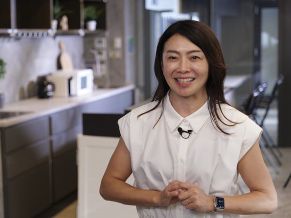 モダンなキッチンで笑顔の人物が立つ。手を前で組んでいる