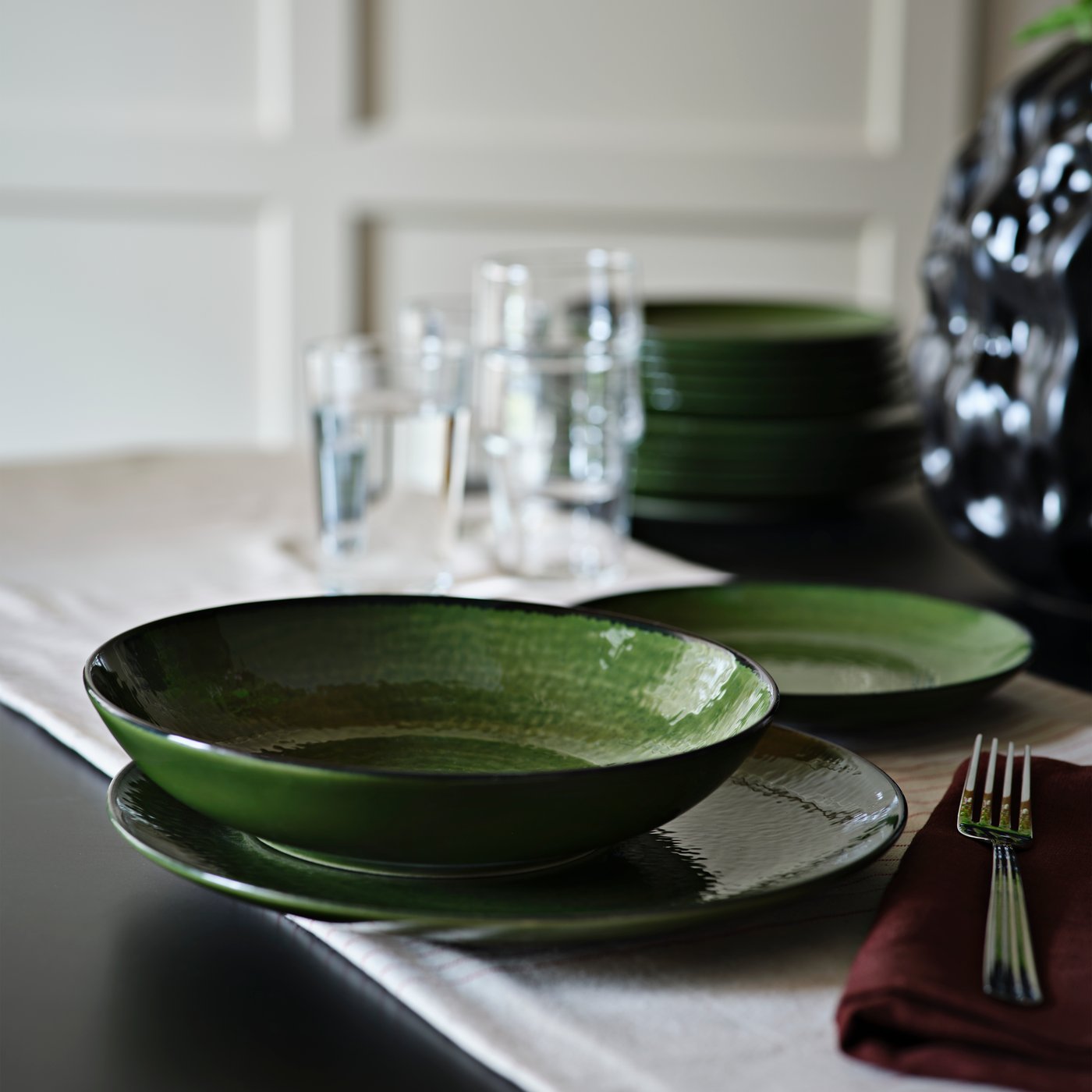 En grön PELARKAKTUS djup tallrik står på ett bord bredvid glas och staplade tallrikar i en elegant matplats.