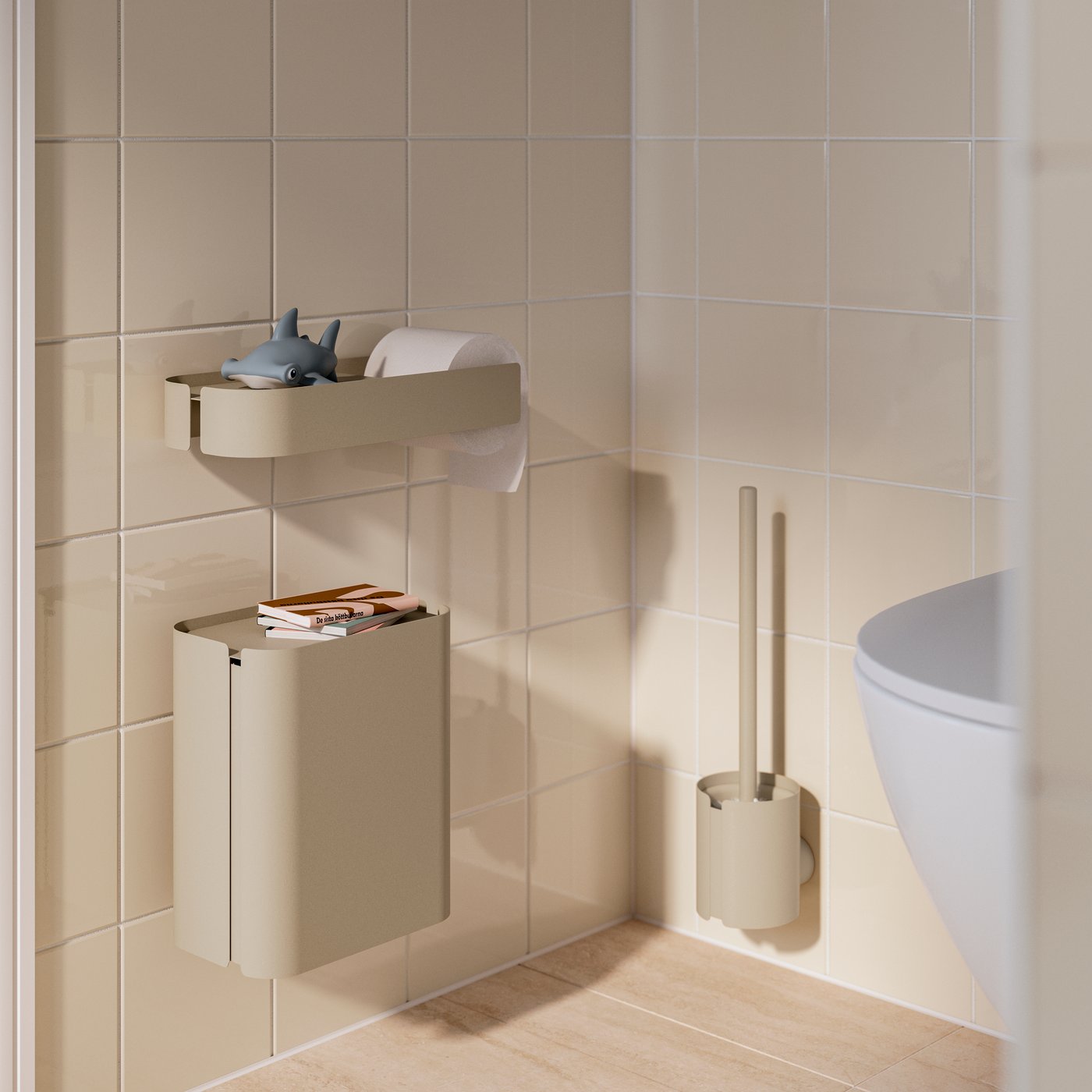 A tiled bathroom corner by a toilet has a grey-beige FLORSJÖN waste bin mounted on the wall, with books on its recessed lid.