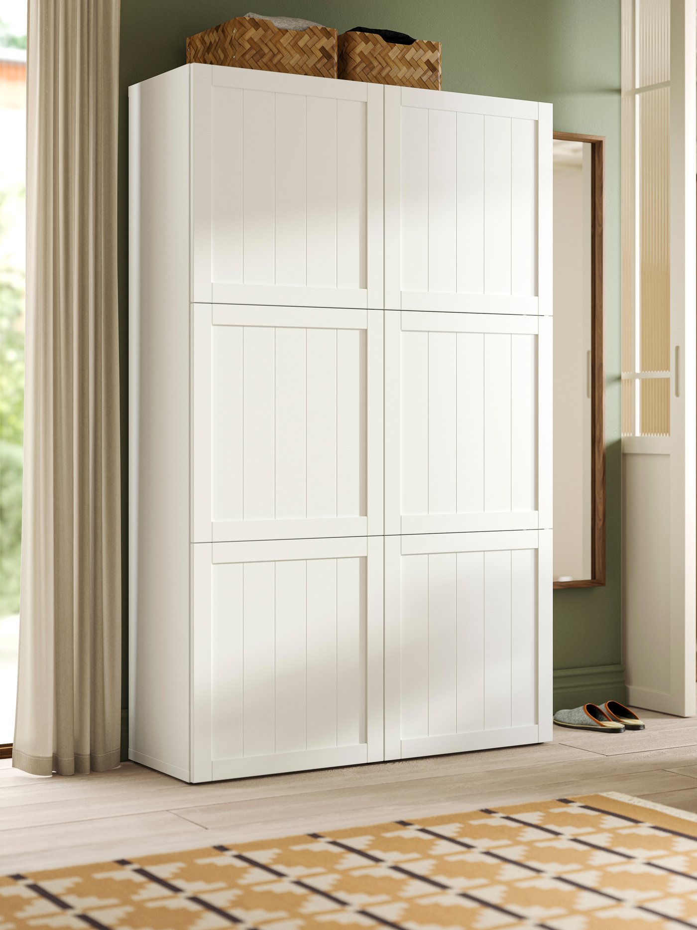 A white/PIPMAKARE white BESTÅ storage combination with 6 doors in a bright room with two baskets on top and a mirror by it.