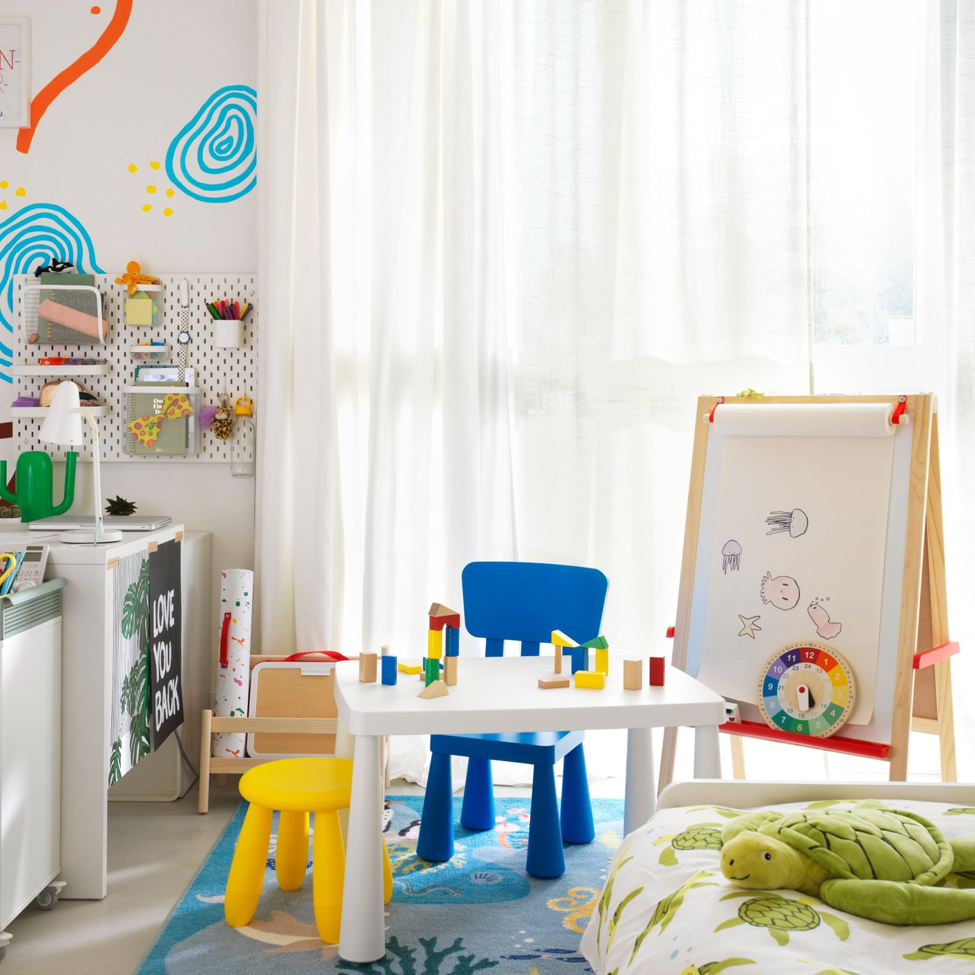 Un dormitori infantil compartit amb uns quants mobles infantils MAMMUT a prop d'un escriptori MICKE blanc i un carretó ÖVNING.