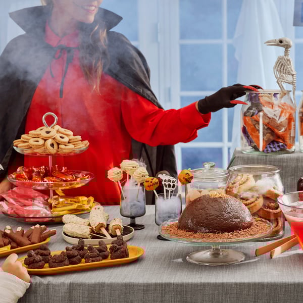 Eine verkleidete Person steht hinter einem Halloween Buffet. 
