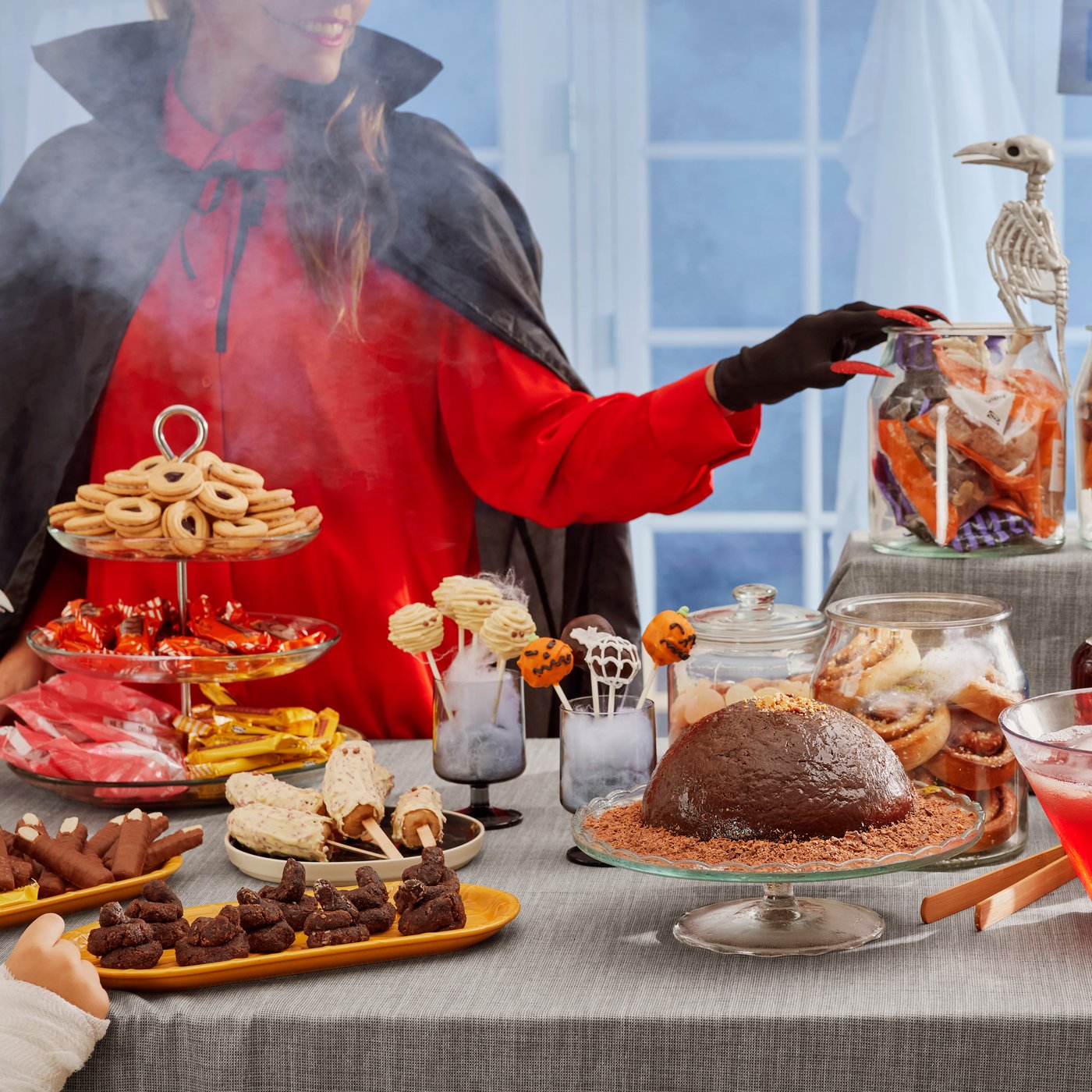 Eine verkleidete Person steht hinter einem Halloween Buffet. 