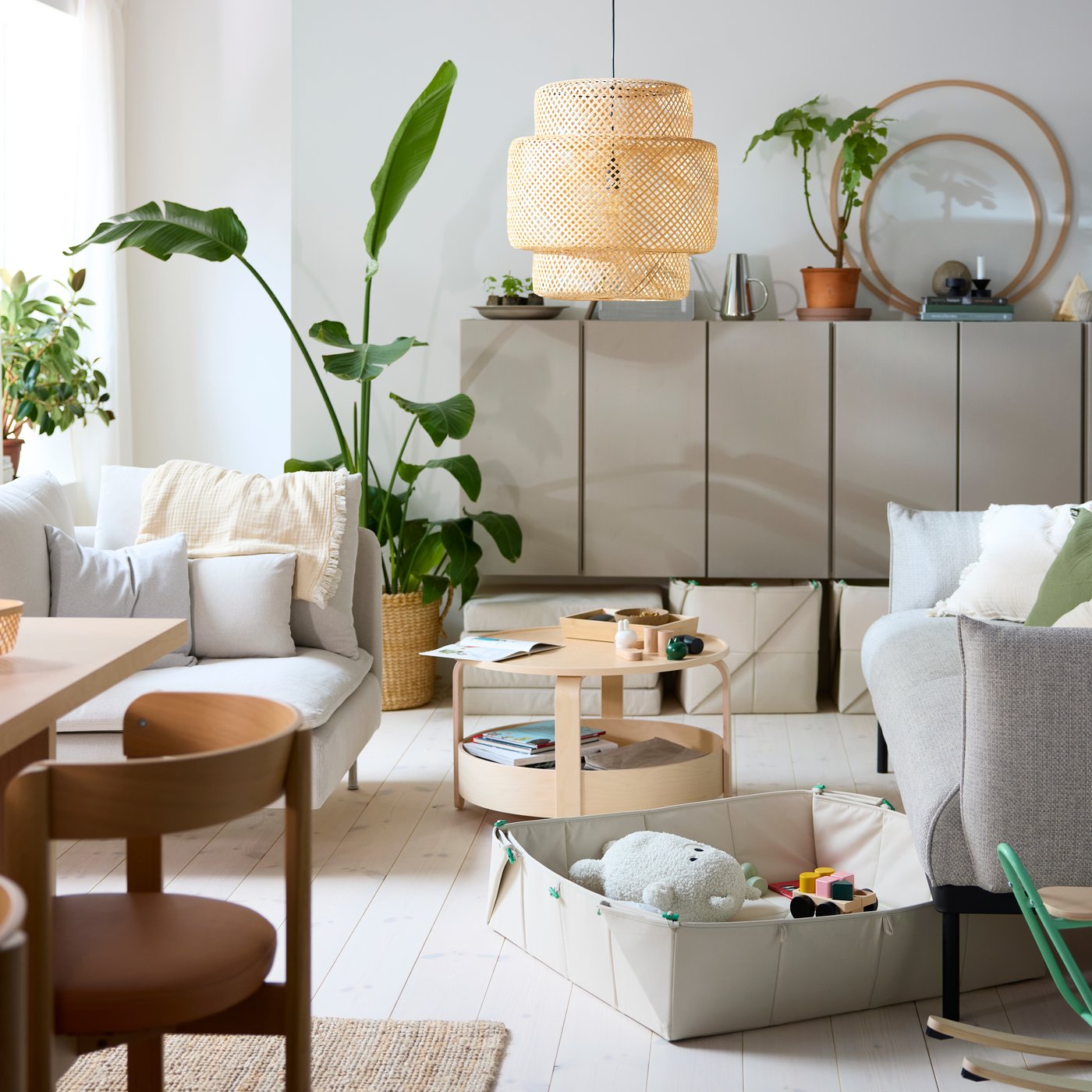 A GREJSIMOJS mat/storage box filled with toys is set near an ÄPPLARYD sofa and BORGEBY coffee table in a bright living room.