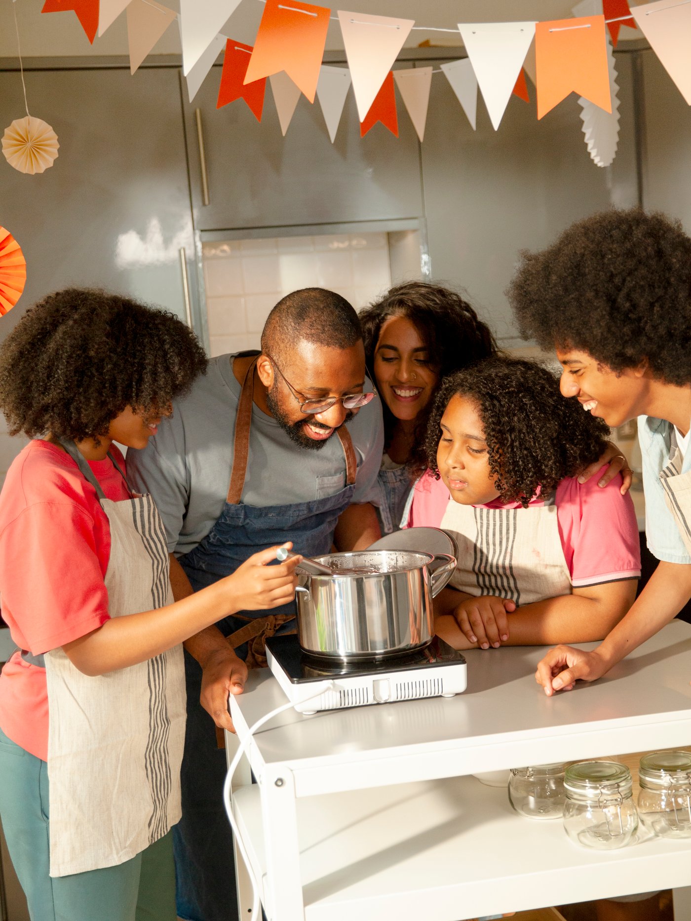 Les cinq membres d’une famille sont autour d’une casserole IKEA 365+ posée sur une table de cuisson mobile à induction TILLREDA.