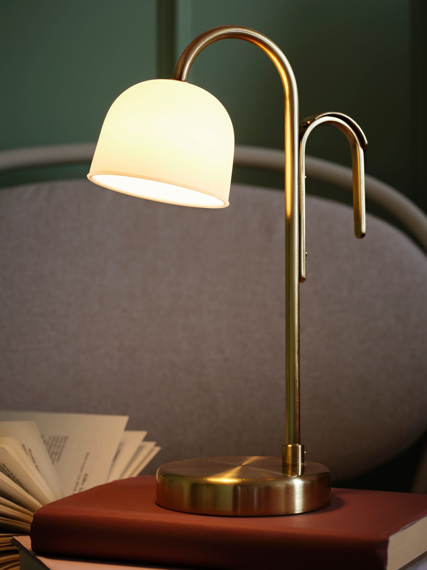 Lampa przenośna TVÅMASTAD stojąca na książce leżącej na fotelu.