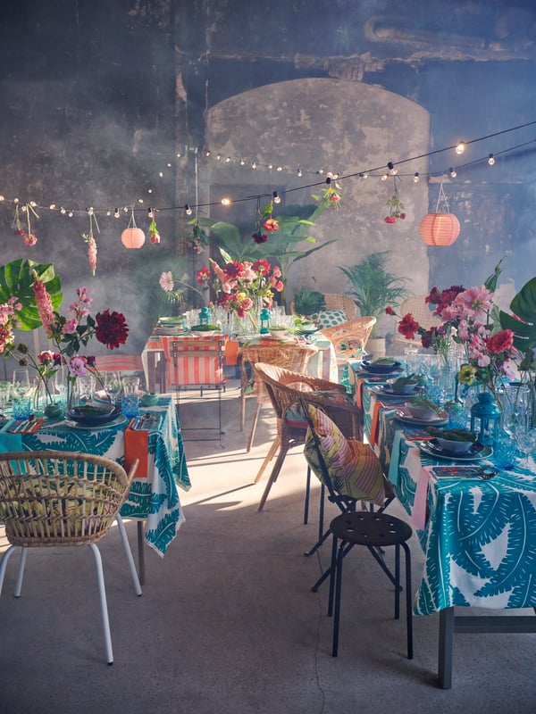 Interior with set tables with lengths of UGGLEMOTT fabric as tablecloths, a criss-cross of SOLVINDEN lighting chains above.